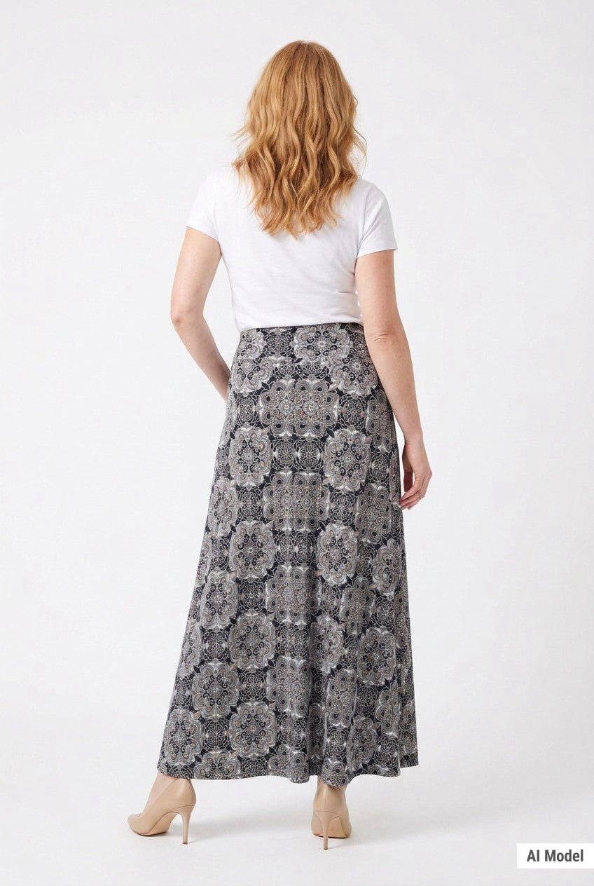 Red-haired female model shown from behind wearing a black medallion-print knit maxi skirt with a white tee and nude heels.