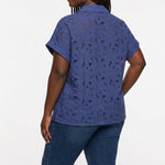 Back view of a plus-size model wearing a navy blue short-sleeve eyelet button-front blouse with floral cutwork detail,