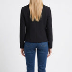 Back view of a blonde woman wearing a black cropped long-sleeve crepe jacket with seam detailing, paired with blue jeans.