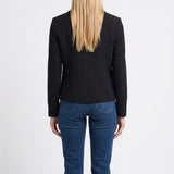 Back view of a blonde woman wearing a black cropped long-sleeve crepe jacket with seam detailing, paired with blue jeans.