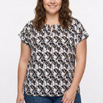 Plus-size model wears a short-sleeve pullover top with navy, taupe, and white abstract print and grommet neckline detail,