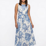 Woman wearing a sleeveless white chiffon maxi dress with blue floral toile print, pleated neckline, and self-tie belt; front