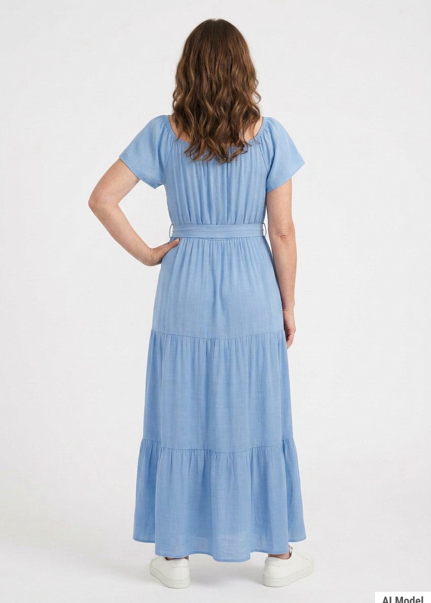 Woman wearing a light blue short-sleeve tiered maxi dress with a tie waist belt, shown from the back; white sneakers visible.