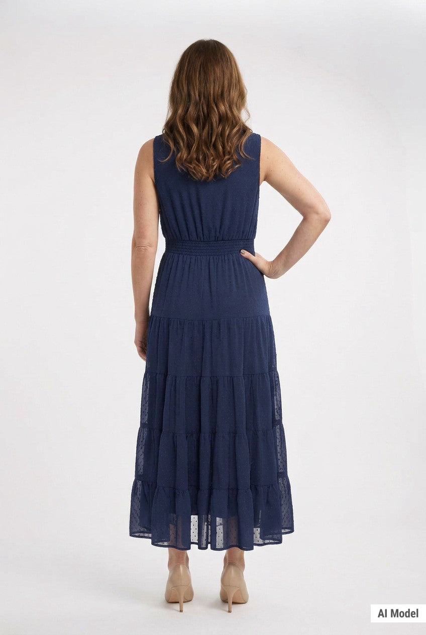 Back view of a woman in a navy sleeveless swiss dot tiered maxi dress with smocked waist, paired with nude heels.