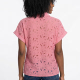 Woman shown from back wearing a pink short-sleeve eyelet button-front blouse with floral cutwork detail, paired with dark
