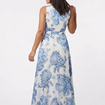White chiffon sleeveless maxi dress with bold blue toile floral print and self-belt, shown from the back on a dark-haired