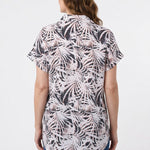 Back view of a woman wearing a short rolled-sleeve button-front blouse in black and blush palm leaf print, paired with blue