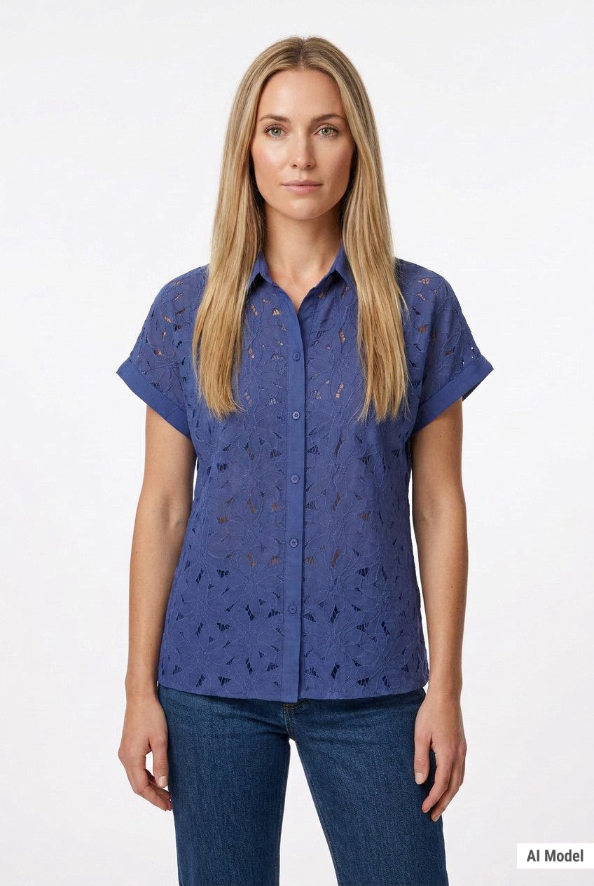 Blonde female model wearing a blue eyelet button-front short-sleeve blouse with floral cutwork detail, paired with dark