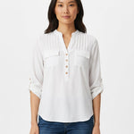 Woman wearing a white popover blouse with pintuck yoke, dual chest pockets, roll-tab sleeves, and tan buttons; front view,