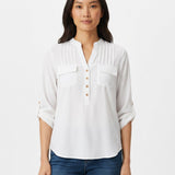 Woman wearing a white popover blouse with pintuck yoke, dual chest pockets, roll-tab sleeves, and tan buttons; front view,
