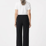 Back view of black wide-leg pull-on pants with elastic waistband on a gray-haired woman wearing a white tee, full-length