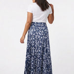 Back view of a dark-haired model wearing a navy blue floral-print knit maxi skirt with a flared hem, paired with a white tee