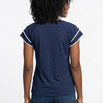 Back view of a woman wearing a navy blue double-layer V-neck blouse with white pom-pom trim on flutter sleeves, paired with