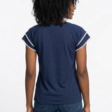 Back view of a woman wearing a navy blue double-layer V-neck blouse with white pom-pom trim on flutter sleeves, paired with