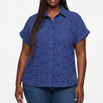 Plus-size model wears a navy blue short-sleeve eyelet button-front blouse with floral cutwork pattern; front view, waist up.