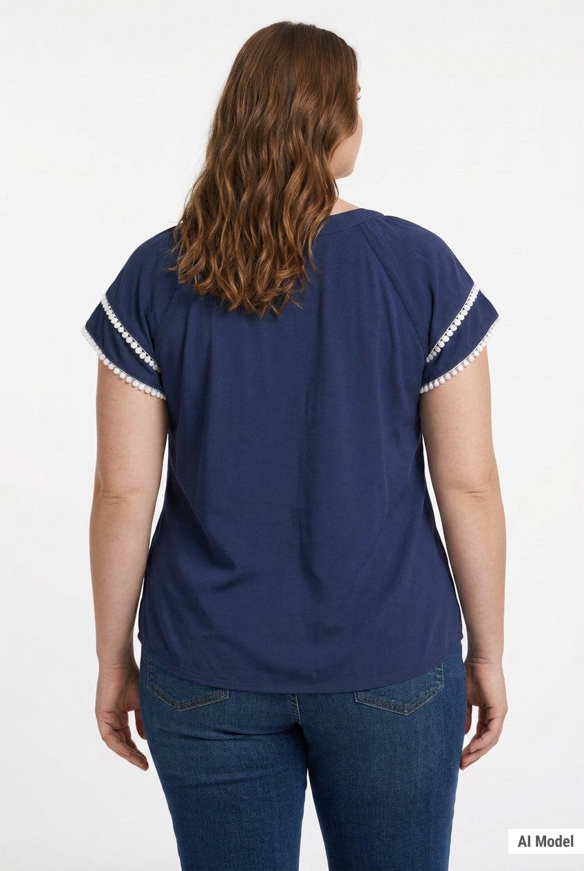 Plus-size model shows back view of navy blue short-sleeve popover blouse with white pom-pom trim on flutter sleeves, paired
