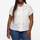 Plus-size model wears a white short-sleeve eyelet button-front blouse with floral cutwork detail; front view, waist up.