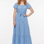 Redhead woman wearing a light blue short-sleeve tiered maxi dress with square neckline and tie waist belt; front view.