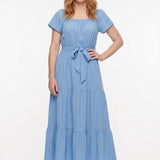 Redhead woman wearing a light blue short-sleeve tiered maxi dress with square neckline and tie waist belt; front view.
