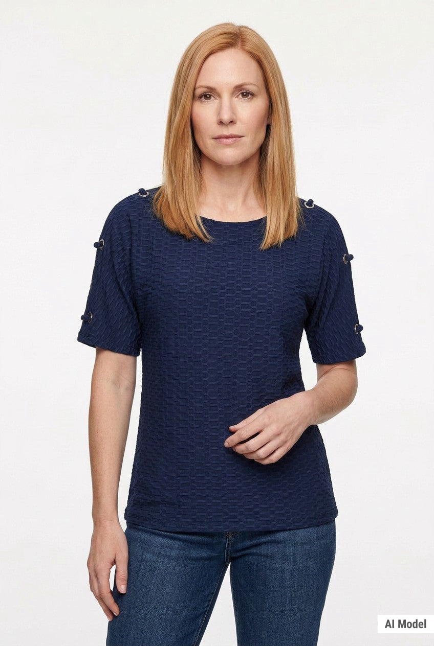 Woman wearing a navy honeycomb-textured short-sleeve tunic with grommet shoulder details, paired with dark jeans; front