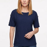 Woman wearing a navy honeycomb-textured short-sleeve tunic with grommet shoulder details, paired with dark jeans; front