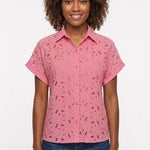 Woman wearing a pink short-sleeve eyelet button-front blouse with collar and cuffed sleeves, paired with dark jeans; front